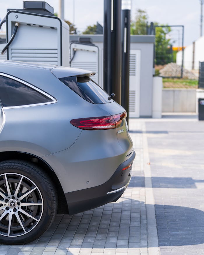 Sleek gray electric car charging at a modern station during the day.